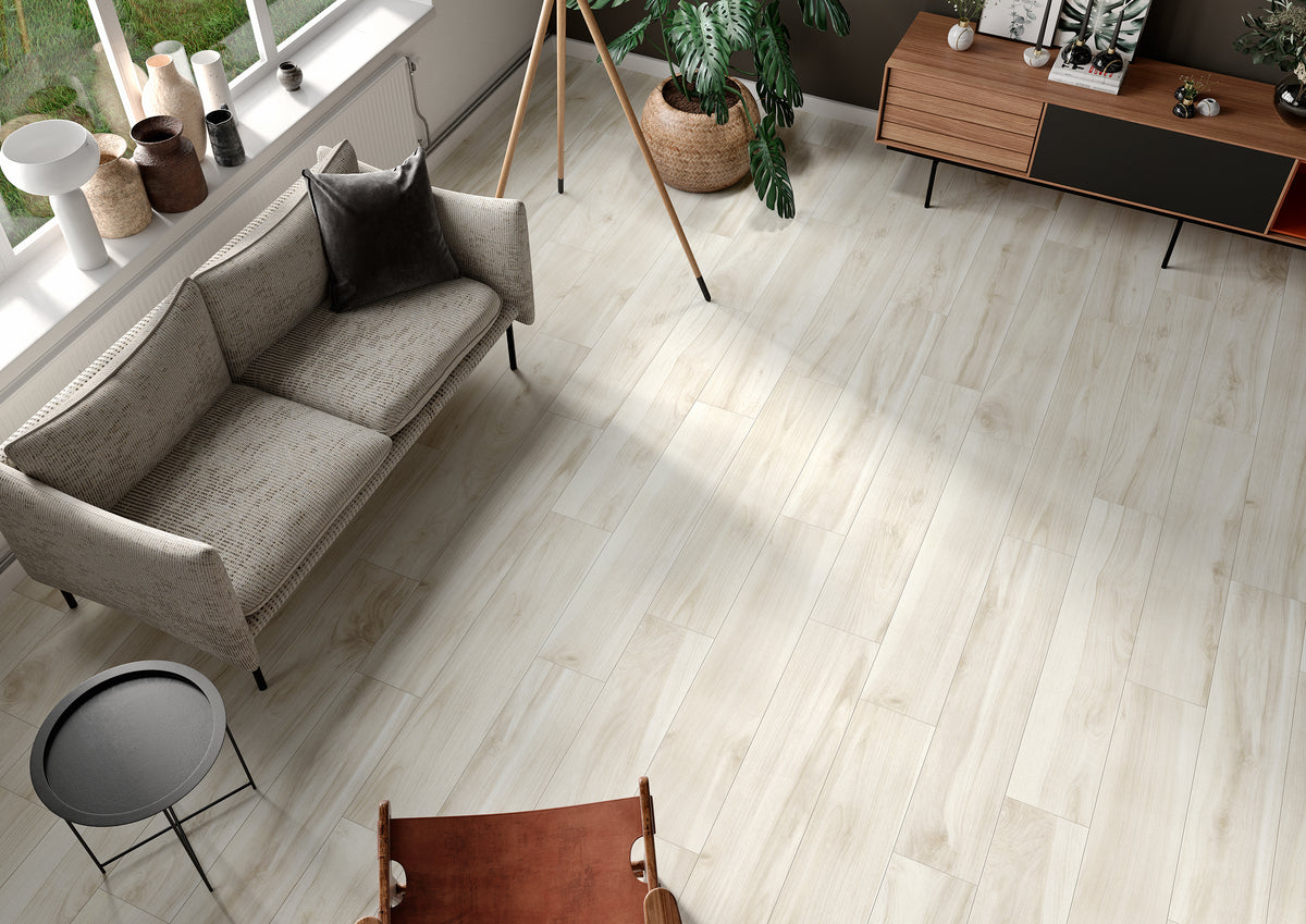 Wood-look porcelain floor tiles installed in a modern living room setting with a gray sofa, wooden sideboard, and plants.
