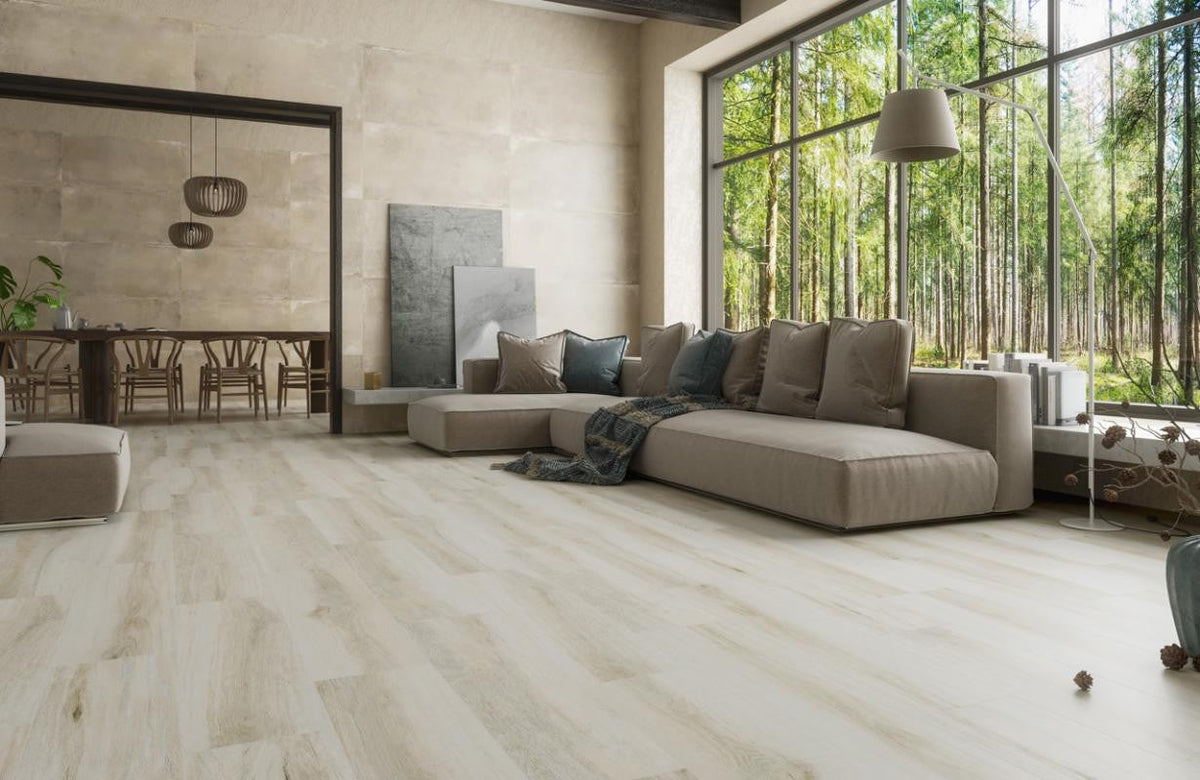 Open living room with a gray sectional sofa and floor-to-ceiling windows on Louvre Cenere 10x40 light oak-look porcelain plank tile