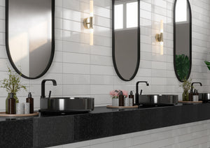 Modern bathroom vanity area with two black vessel sinks, matte black faucets, oval mirrors with black frames, and a dark stone countertop against a white tiled wall.