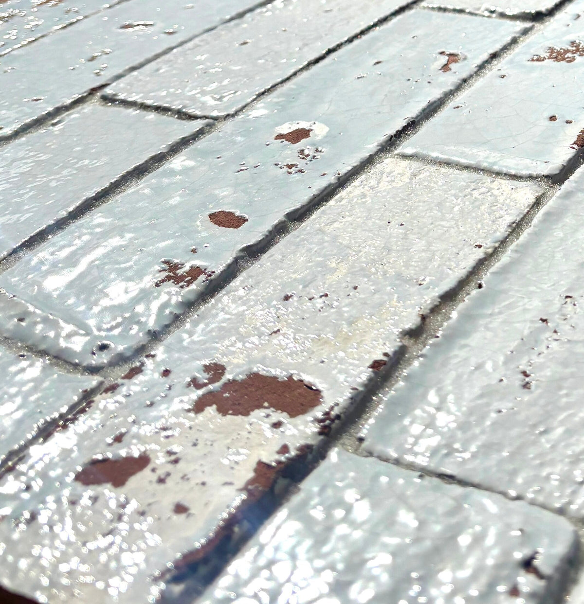 Close-up of Artesano Cozumel Blue glossy clay brick tile with light on the crackled pale blue glaze and exposed terracotta